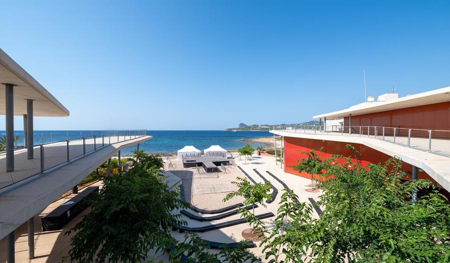 Vista exterior del Auditorio Caló de s’Oli, un moderno espacio cultural junto al mar en la costa de Ibiza, con arquitectura contemporánea, amplias ter