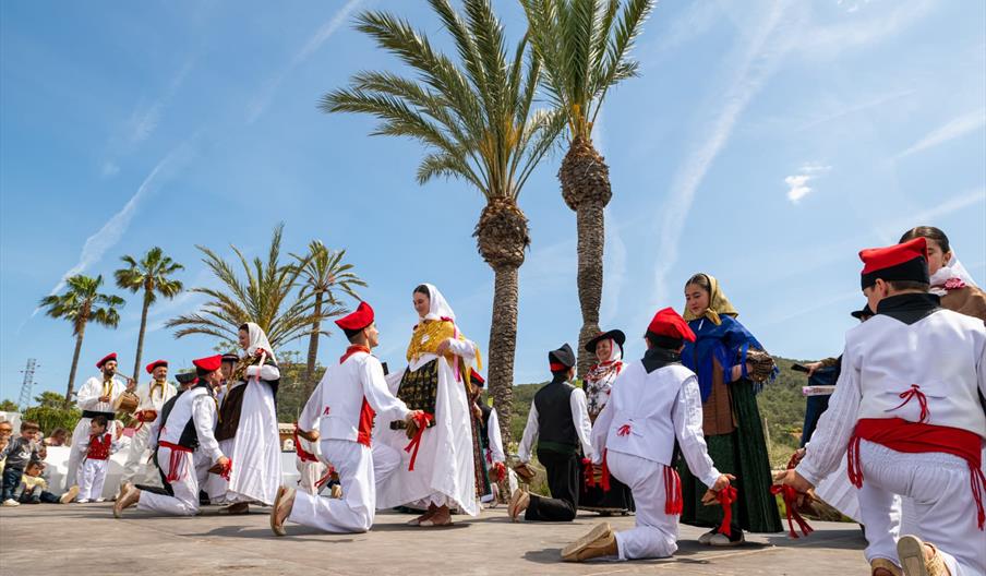 Hombres y mujeres ataviados con la vestimenta tradicional ibicenca realizan el ball pagès en un emplazamiento al aire libre.