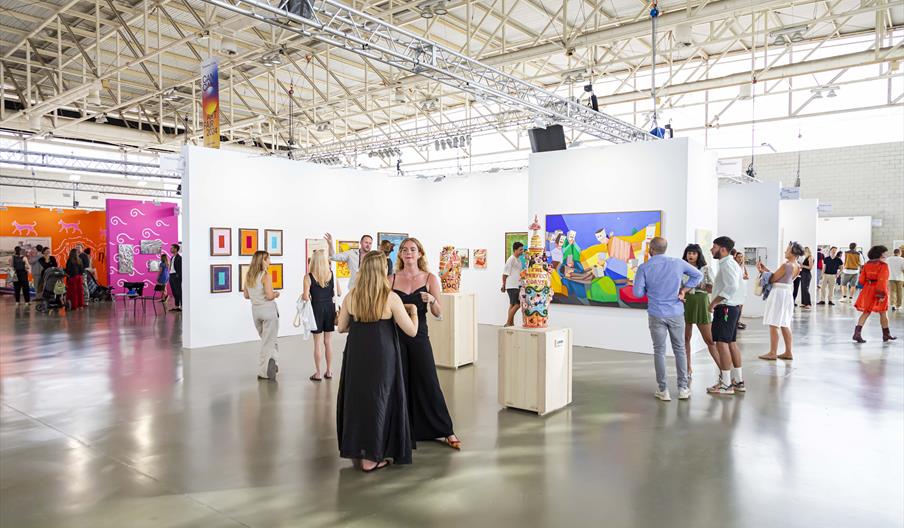 Sale de exposiciones con obras de arte dentro del evento Can Art. Aparece mucha gente charlando y observando las obras.