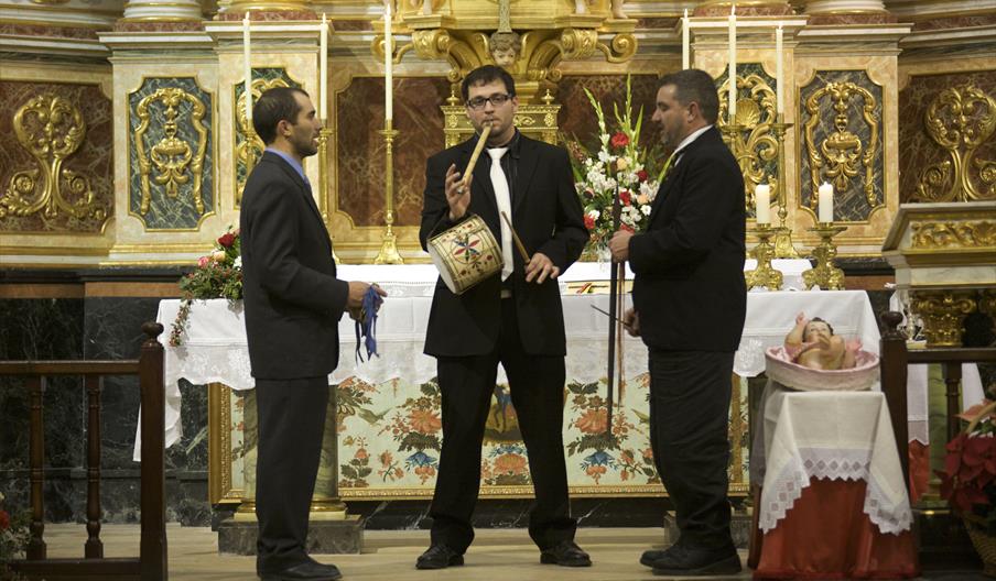 Tres hombres tocan instrumentos diversos en el altar de una iglesia durante los Caramelles de Nadal.
