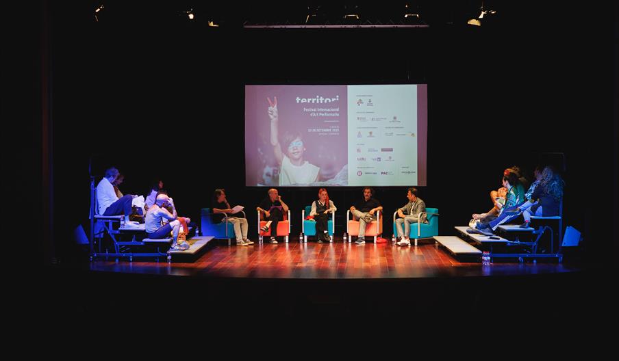 Momento de un acto dentro del Festival Territori. Aparecen varias personas sentadas en sillones y una especie de escaleras o gradas hablando entre sí.