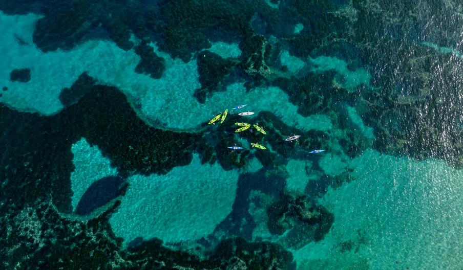Vista aérea de personas practicando kayak sobre aguas cristalinas y fondos marinos turquesa en la costa de Ibiza.