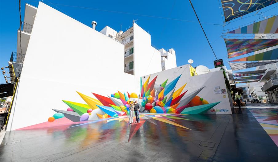 Pintura mural de muchos colores en la que se ven formas geométricas, como si fueran cristales de algún mineral, y otras piedras redondas.El fondo es b