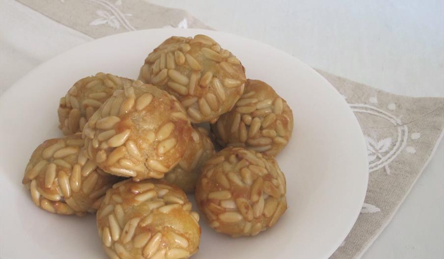 Primer plano de varios panellets tradicionales cubiertos de piñones dorados y brillantes, pequeños dulces elaborados con almendra y azúcar, presentado