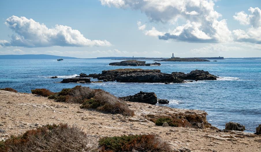 Vista de los islotes de Es Freus, con formaciones rocosas, aguas cristalinas y el faro al fondo bajo un cielo abierto entre Ibiza y Formentera.