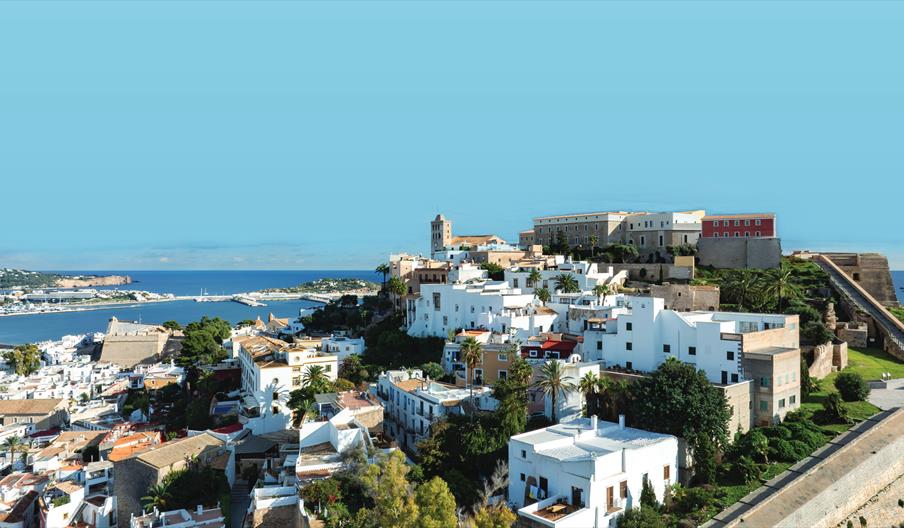 Se ve la muralla de la ciudad amurallada de Dalt Vila, con la catedral y los baluartes sobre la ciudad de Ibiza y con el Mediterráneo al fondo.