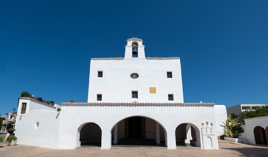 Iglesia con dos cuerpos, uno abajo con tres arcos de medio punto, uno central más ancho. A la derecha hay un saliente con 3 cruces negras. El cuerpo s