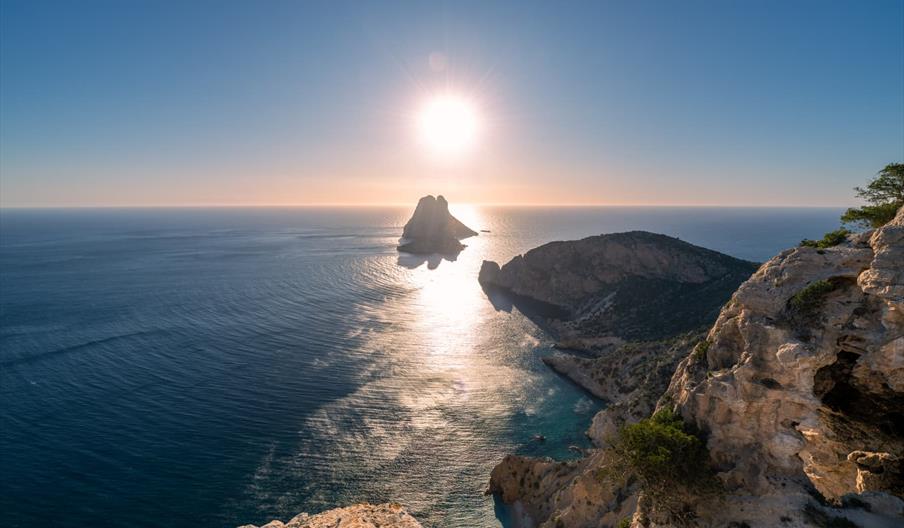 Vista de la Reserva Natural de Es Vedrà y Es Vedranell al atardecer, con acantilados y el mar Mediterráneo reflejando la luz del sol frente a la costa