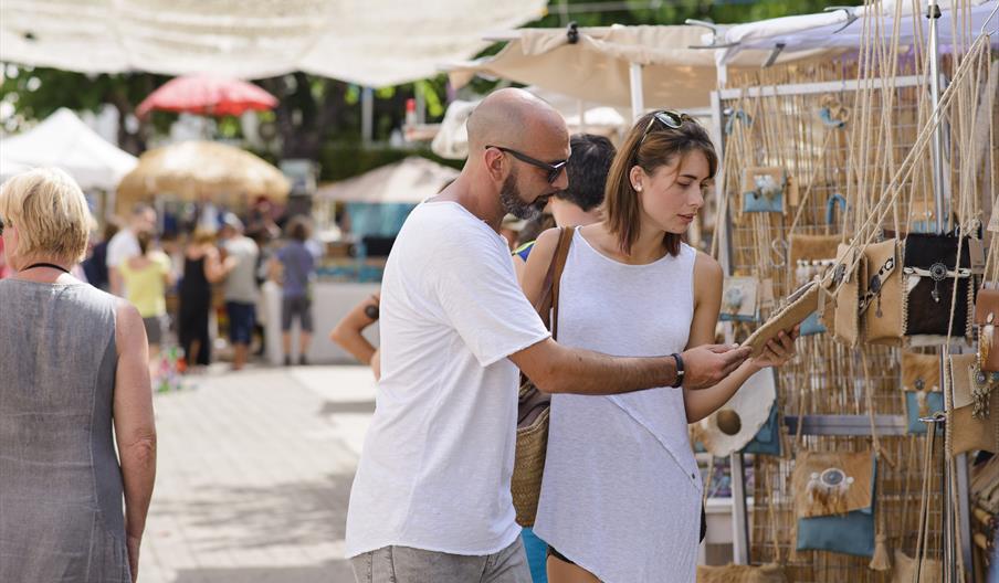 Personas recorriendo el mercadillo de artesanía de Sant Joan, descubriendo productos hechos a mano y creaciones locales en un ambiente tradicional y a